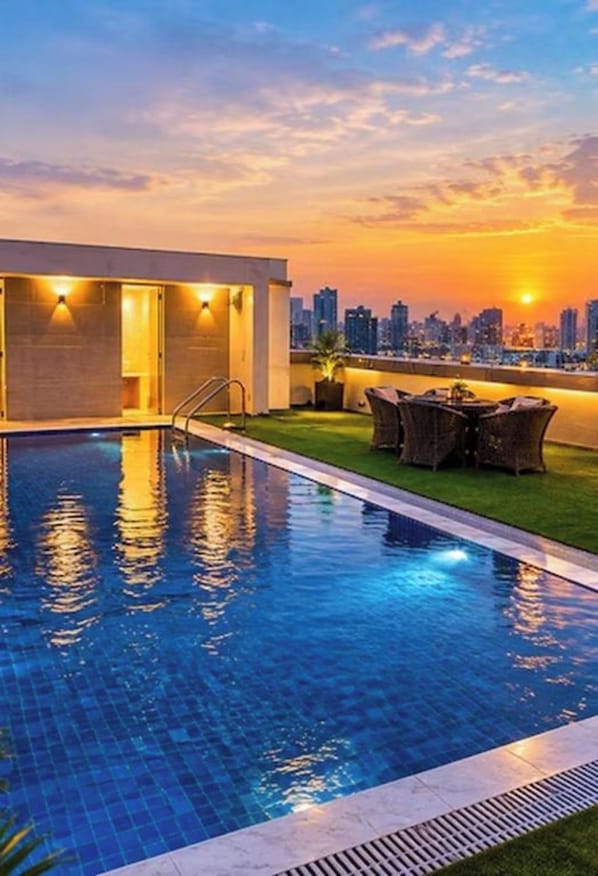 A swimming pool with a city skyline view at sunset. - Hotel Sakura Gold (Gurugram)