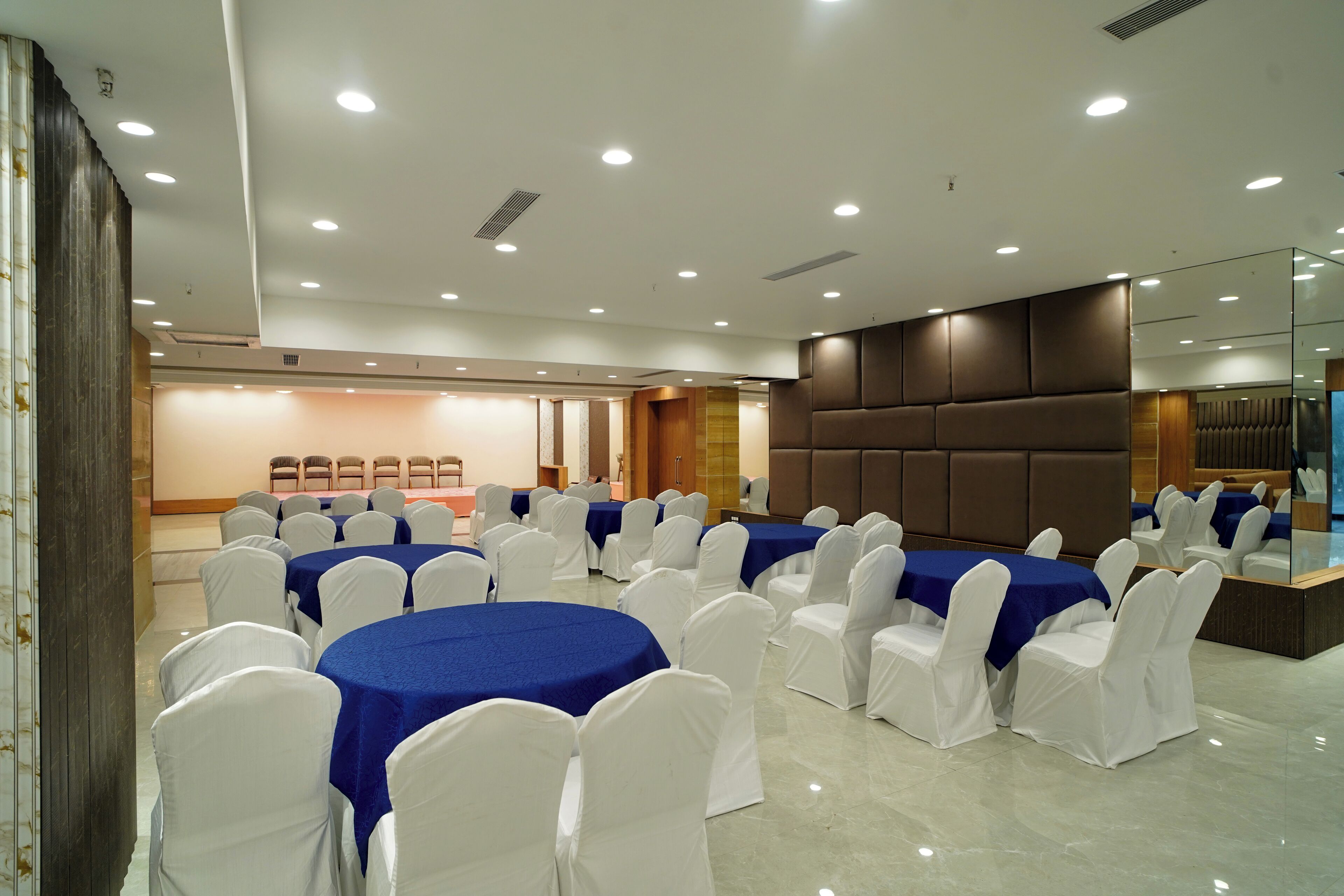 A conference room with round tables covered in blue tablecloths and white chairs, equipped with ceiling lights and a modern design.