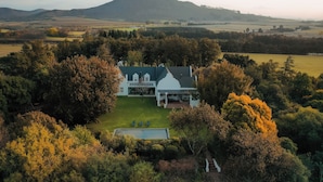 A large house surrounded by trees and fields, with a mountain in the background. - Luxury, self-catering Manor with 6 bedrooms, views of mountains & vineyards (Klapmuts)