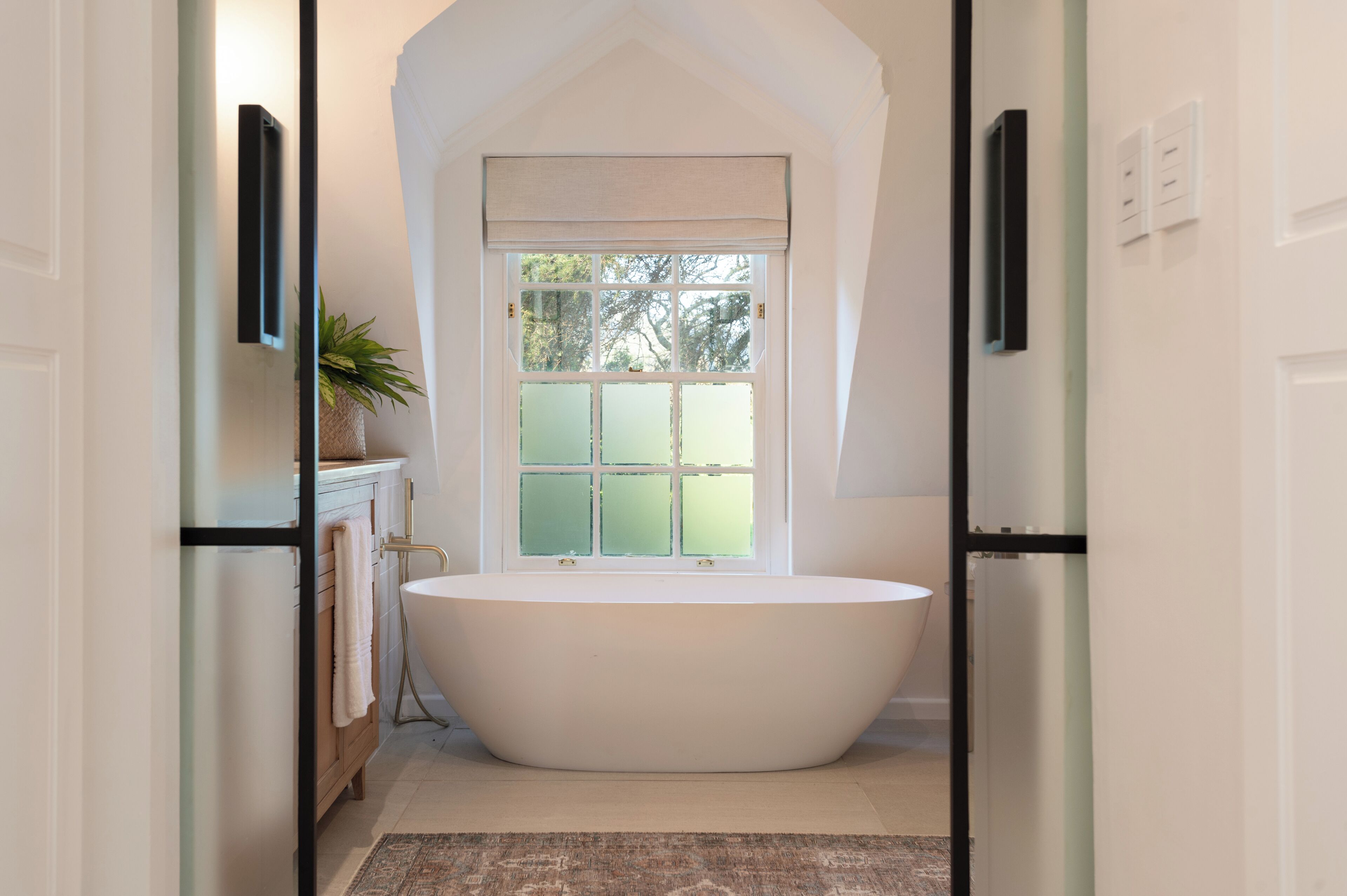 Un baño moderno con una bañera independiente, un ventanal con vistas a árboles y un diseño minimalista.