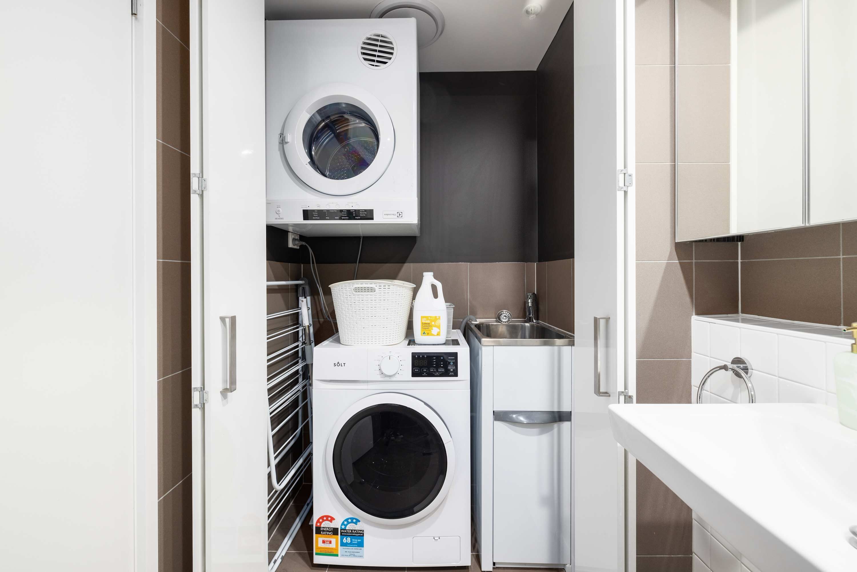 Een kleine wasruimte met een voorlader wasmachine en droger, een klein wastafeltje en een wit aanrecht.