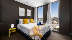 Une chambre avec un grand lit, une table de chevet et deux citations encadrées au mur, offrant une vue sur la ville par une grande fenêtre.