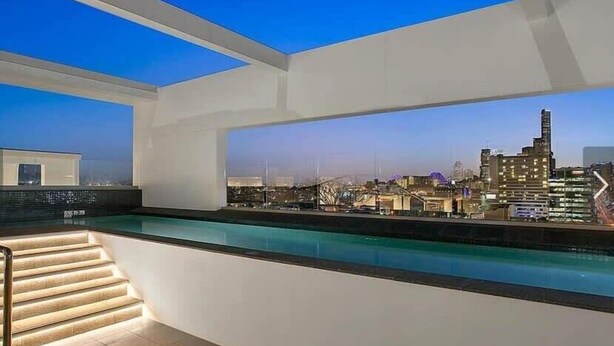 Une piscine moderne située sur le toit, offrant une vue sur la ville, avec un escalier et un ciel dégagé.