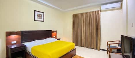 A hotel room with a bed, a television, a desk, and a window with curtains.