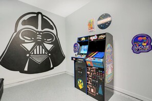 Huoneessa on suuri Darth Vader -aiheinen seinätarra, Capcomin pelihalliarkadikone ja kaksi pelihallipelin julistetta.