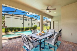 An outdoor patio with a pool, a table with chairs, and a ceiling fan.