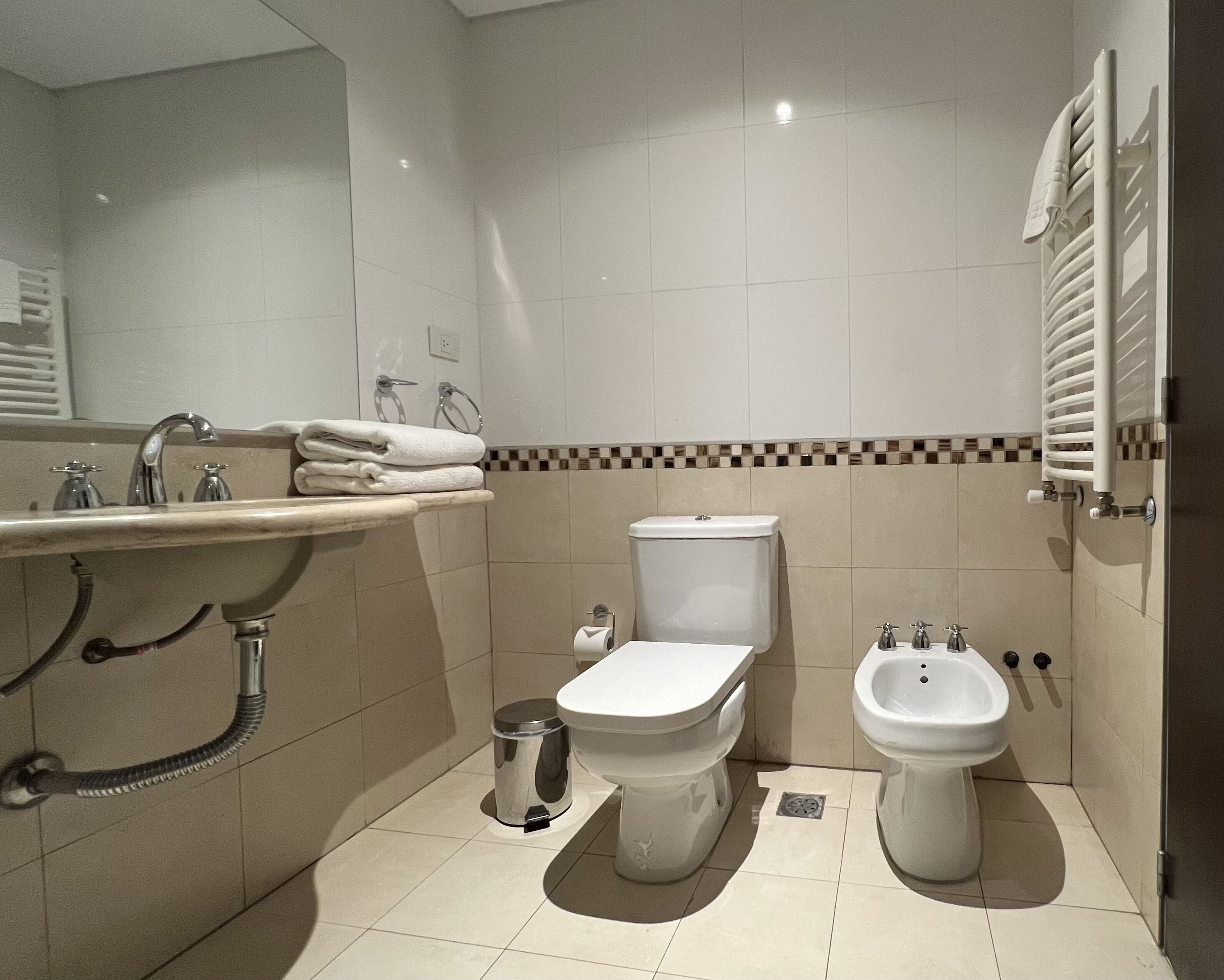 A modern bathroom with a sink, toilet, bidet, and a towel rack.