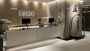 Un mostrador de recepción moderno con un panel de pared de madera, dos monitores, una planta y un ascensor de vidrio.