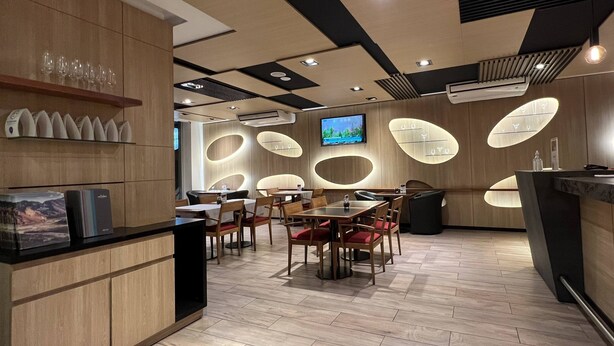 Interior moderno de restaurante con paneles de madera, una zona central de comedor con mesas y sillas, y un televisor montado en la pared.