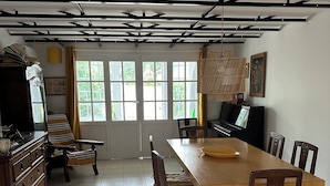 A dining area with a large wooden table, chairs, a piano, and a television.