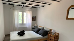 A single bed with a wooden frame, a bedside table with a lamp, a wicker side table, and a window with curtains.