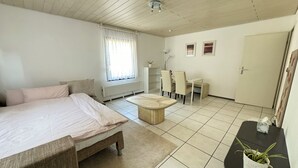 A bedroom with a bed, a small table, a chair, a radiator, a window with curtains, and a door. - H&H Home - Quite and Central Apartment near Park in Sindelfingen (Sindelfingen)