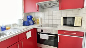 A kitchen with red cabinets, a Bosch oven, a microwave, and a coffee maker. - H&H Home - Quite and Central Apartment near Park in Sindelfingen (Sindelfingen)