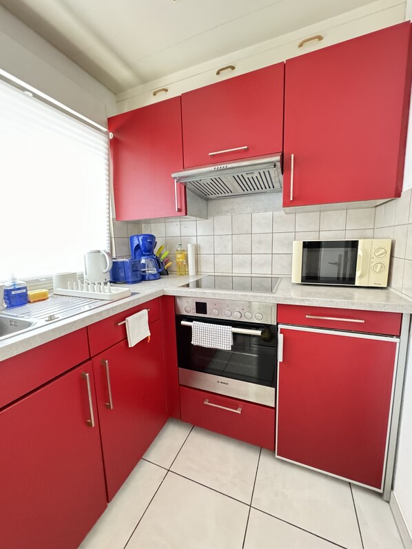 A kitchen with red cabinets, a Bosch oven, a microwave, and a coffee maker. - H&H Home - Quite and Central Apartment near Park in Sindelfingen (Sindelfingen)