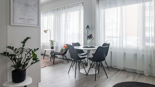 Ein modernes Wohnzimmer mit einem runden Esstisch, schwarzen Stühlen und einem Topfpflanzen.