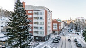 Ein mehrstöckiges Gebäude mit Backstein- und weißen Außenwänden, einem sichtbaren Eingang und einem Parkplatz mit Autos.