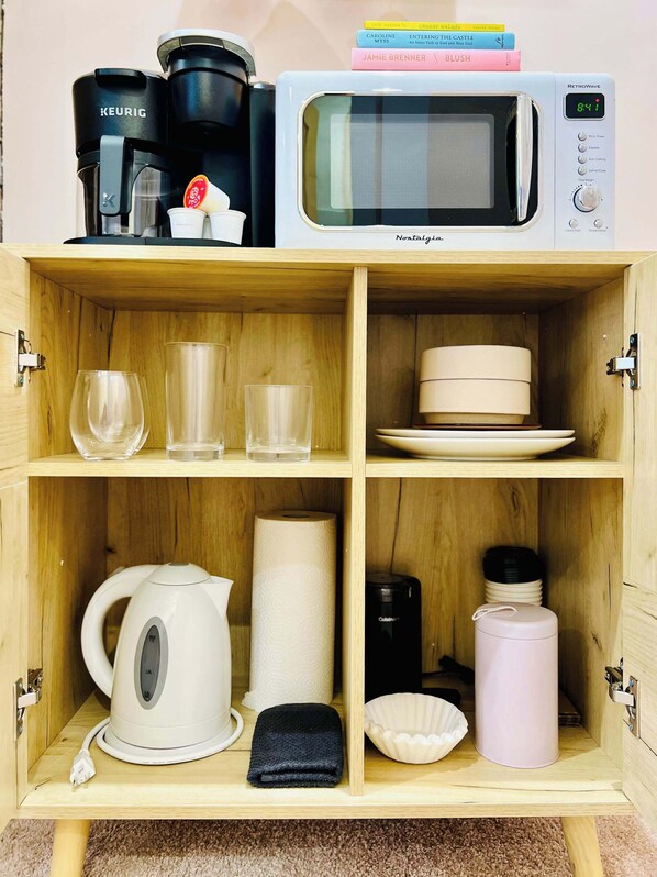 Una kitchenette equipada con cafetera, microondas, hervidor y estantes para almacenamiento.