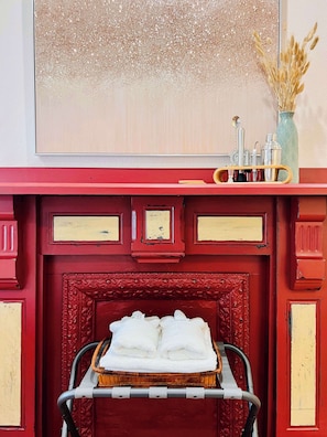 Chimenea de estructura roja con un recipiente que contiene toallas blancas, un florero con flores secas y un espejo en la parte superior.