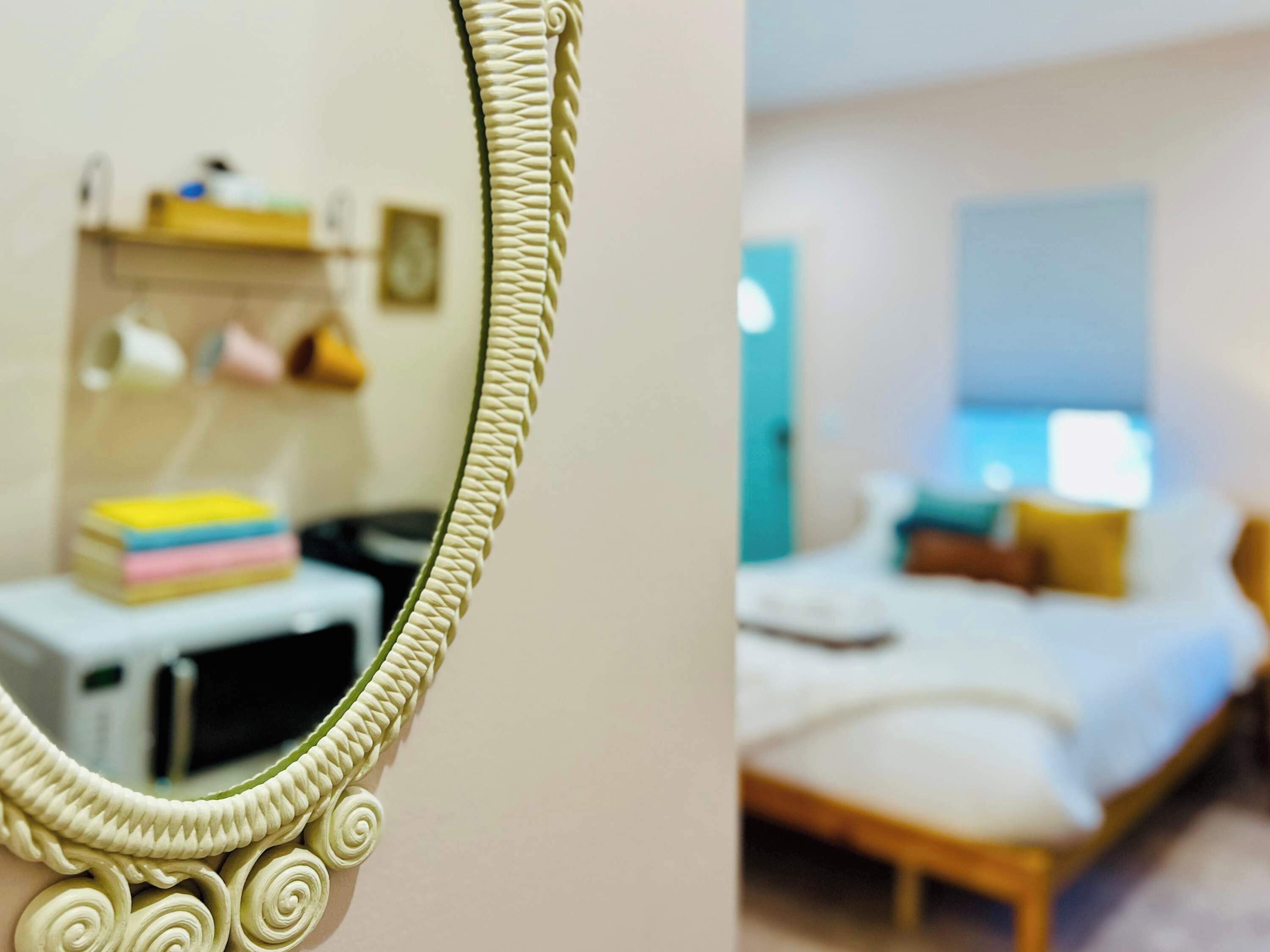 Una habitación con cama, mesita de noche y espejo con marco decorativo.