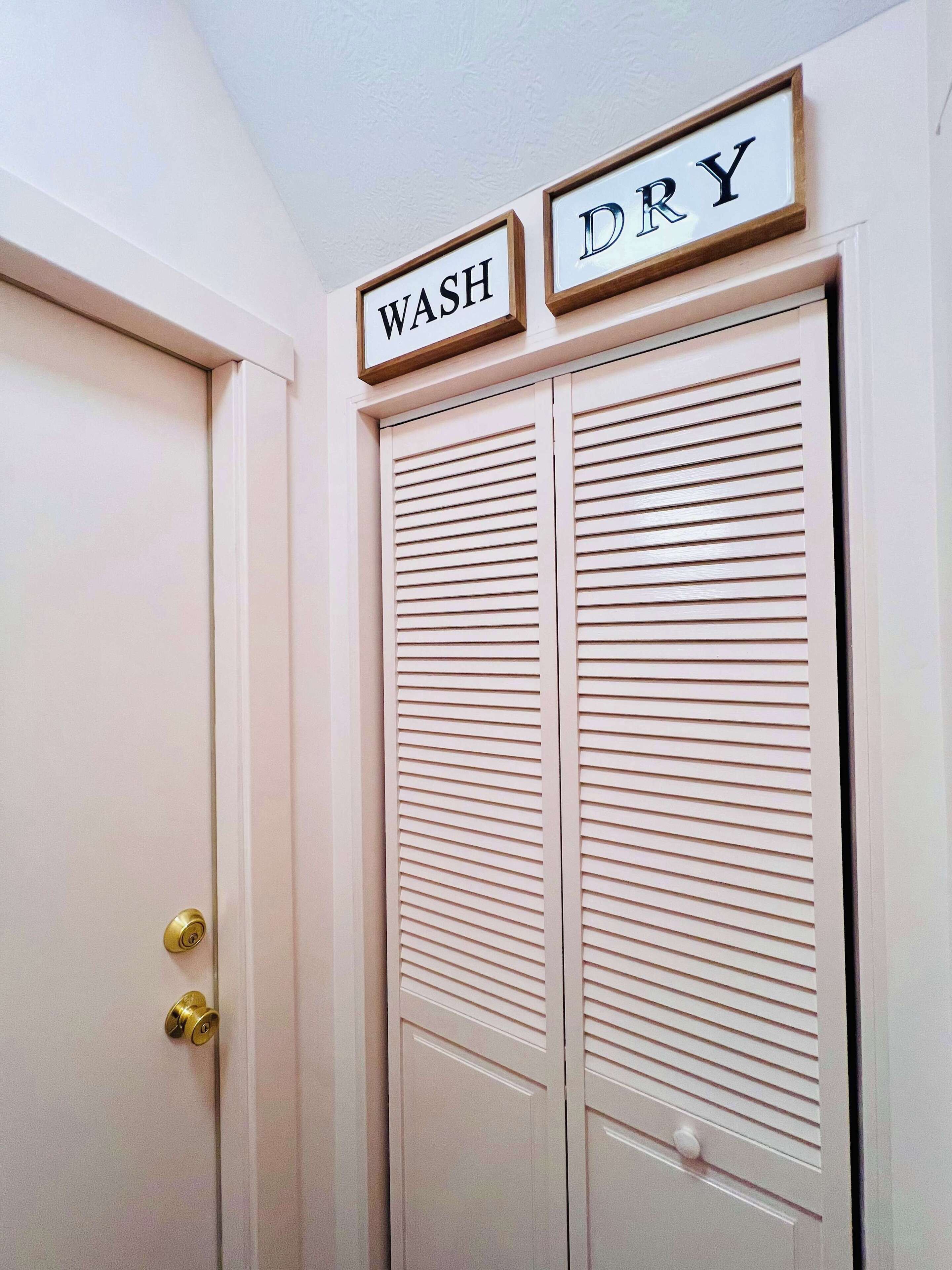 A white door with a brass doorknob and a set of louvered closet doors. Above the doors, there are two framed signs with the words "WASH" and "DRY" in capital letters.