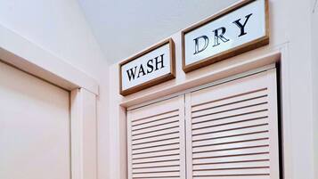A white door with a brass doorknob and a set of louvered closet doors. Above the doors, there are two framed signs with the words "WASH" and "DRY" in capital letters.
