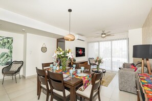 Un salón moderno con comedor, ventilador de techo y un ventanal con cortinas.