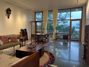 A spacious living room with a sofa, coffee table, and dining table. Large windows offer a view of the outdoors.