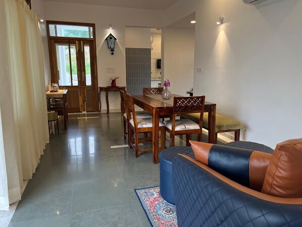 A spacious living area with a dining table, wooden chairs, and a blue sofa with leather cushions.