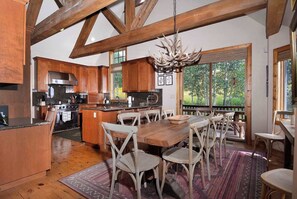 A spacious kitchen with wooden beams, a large island, and a dining area with rustic chairs. - Creek Cove, Gorgeous home, hot tub, very private (Crested Butte)