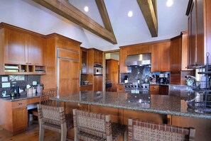 A spacious kitchen with wooden cabinets, granite countertops, and a large island with seating. - Creek Cove, Gorgeous home, hot tub, very private (Crested Butte)
