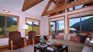 A spacious living room with a large window, a sofa, a chair, and a coffee table. - Creek Cove, Gorgeous home, hot tub, very private (Crested Butte)
