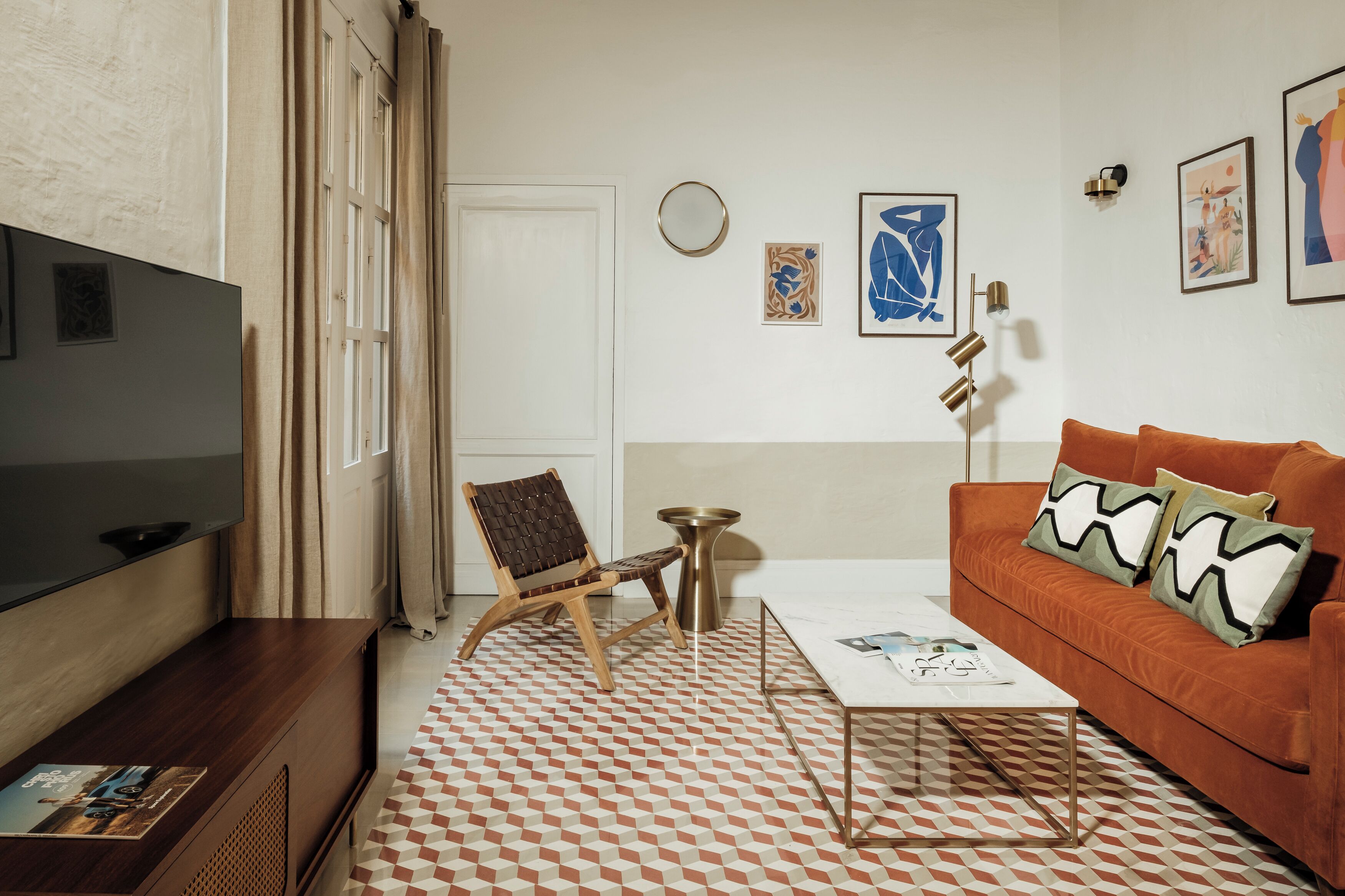 A living room with a flat-screen TV, a brown leather sofa, a patterned rug, and a coffee table.