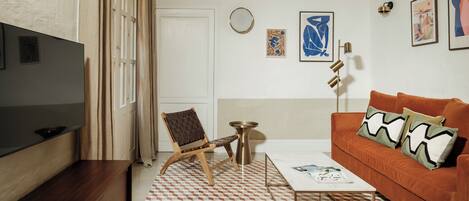 A living room with a flat-screen TV, a brown leather sofa, a patterned rug, and a coffee table.