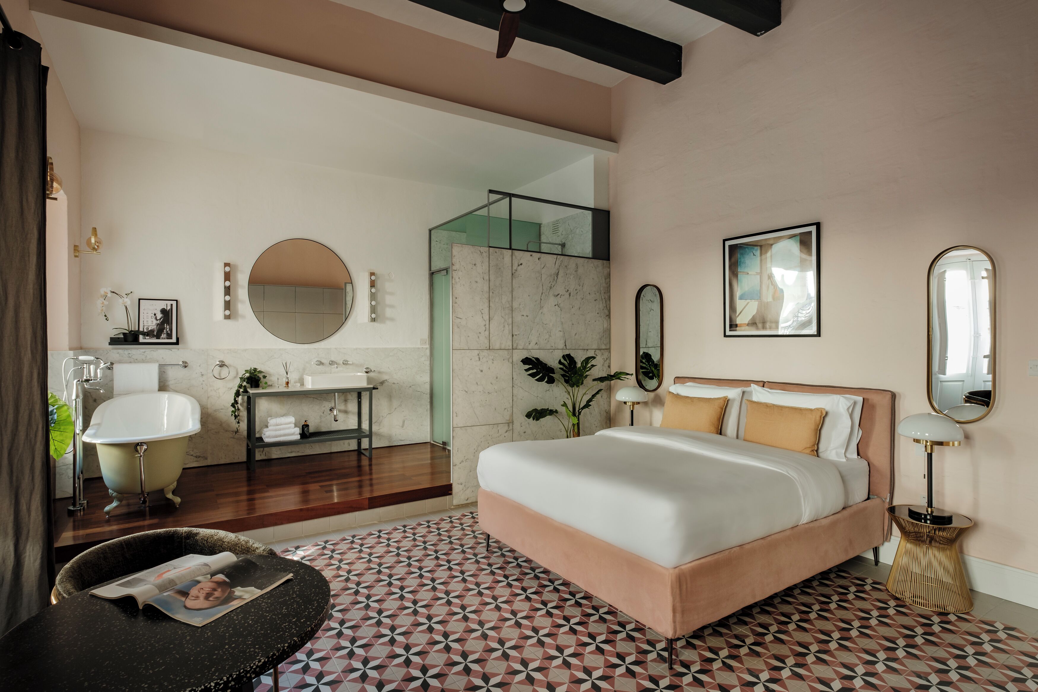 Un dormitorio moderno con una cama grande, un espejo redondo y un baño con bañera y lavamanos.