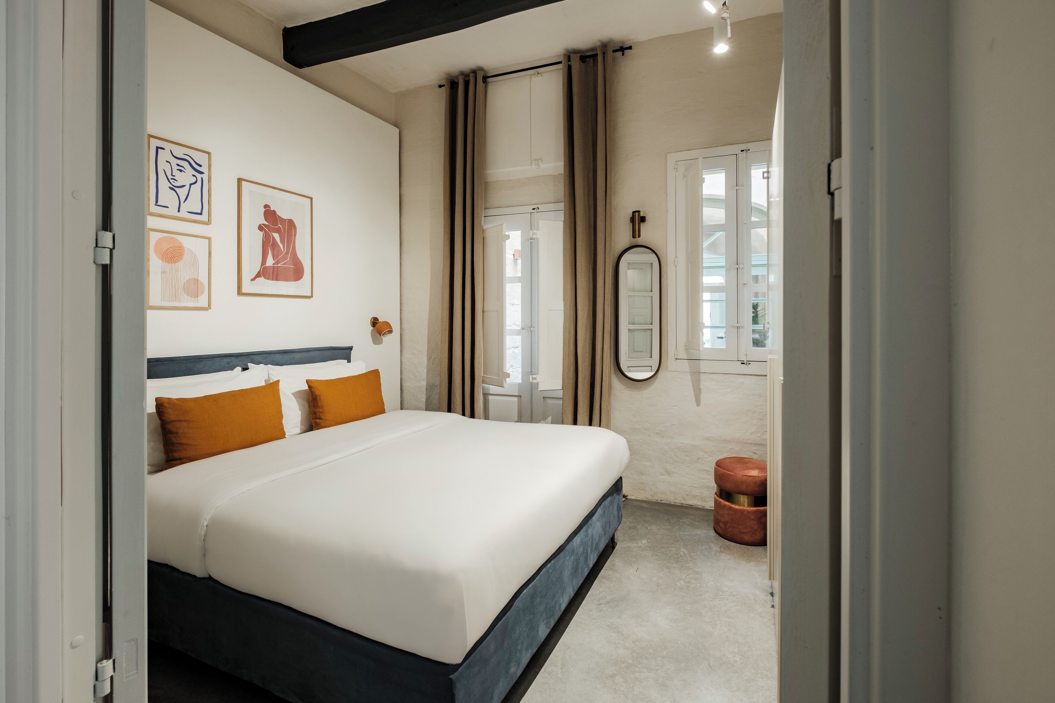 Une chambre à coucher avec un lit, une table de chevet, un miroir et des œuvres d’art accrochées au mur.
