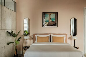 A hotel room with a large bed, two bedside lamps, a potted plant, and a framed picture on the wall.