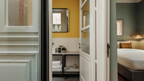 Ein Hotelzimmer mit Bett, Nachttisch, Spiegel und einem Badezimmer mit Waschbecken und Handtuchhalter.