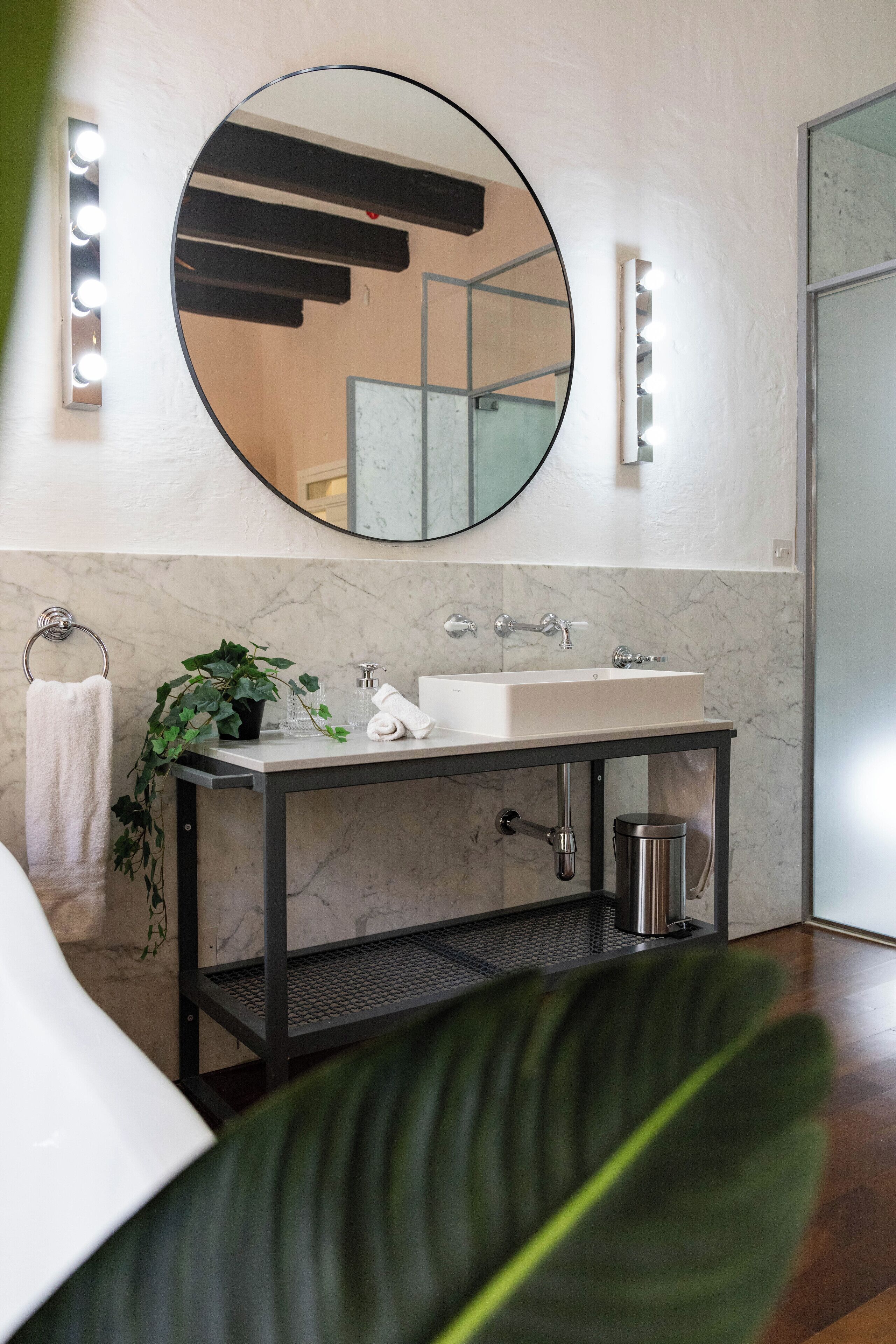 Un baño moderno con un espejo redondo, un lavamanos blanco y una planta en maceta.