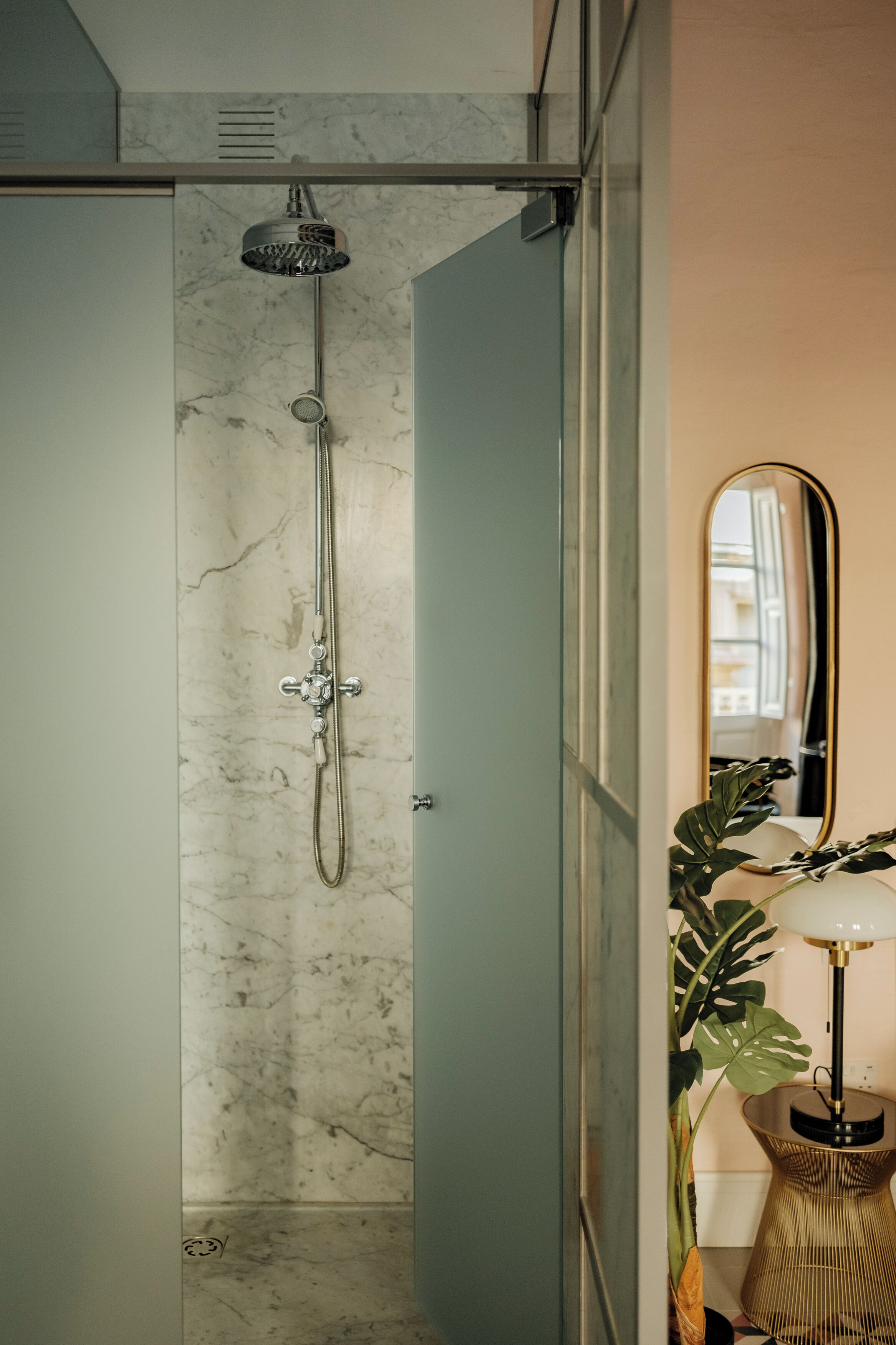 Un baño moderno con ducha, paredes de mármol, un espejo y una planta.