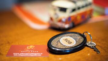 A key fob with the number 308 on a wooden surface, a business card for Hotel Villagaja, and a blurred toy car in the background.