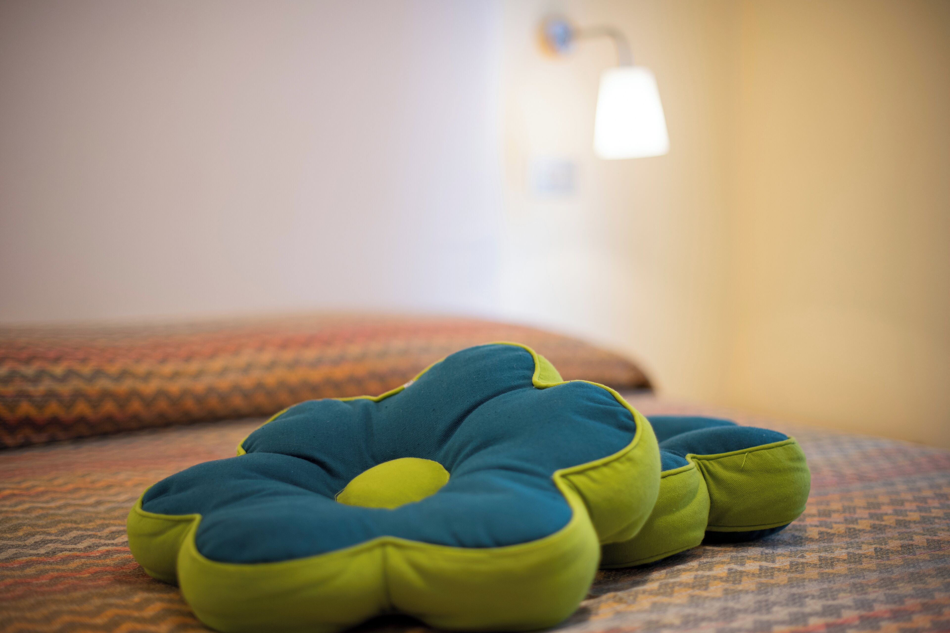 A bed with a patterned bedspread and a blue and green flower-shaped pillow.