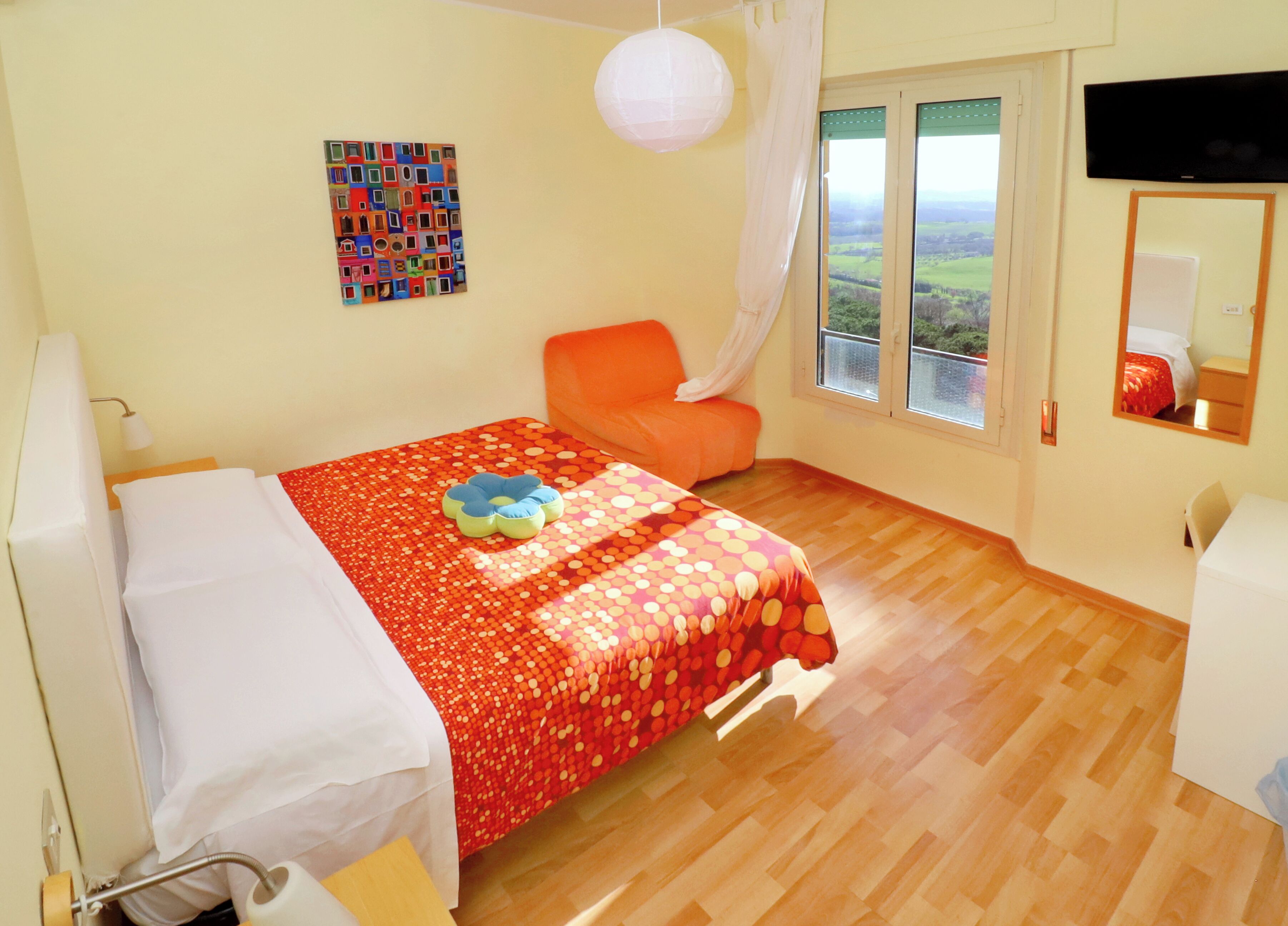 A bedroom with a bed, a chair, a window with a view, a TV, and a mirror.