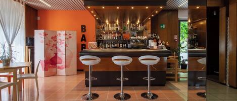 Zona de bar con tres taburetes, barra con botellas y pared decorativa con el letrero 'BAR'.