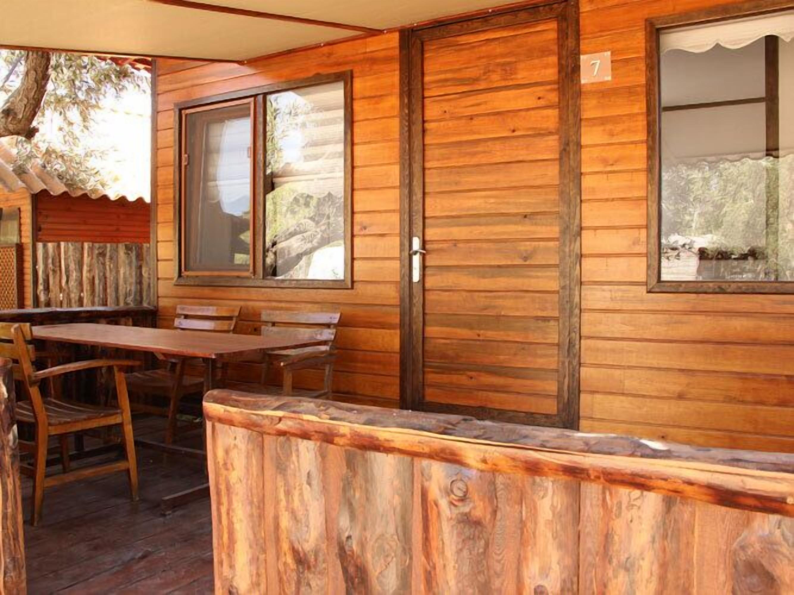 A wooden cabin with a dining area, a large window, and a door.