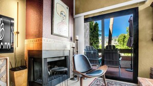 A modern living room with a fireplace, a large window, and a patio area with outdoor furniture. - Palm Springs Getaway - A Ryson Property (Palm Springs)