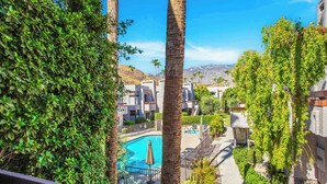 A pool area with a clear blue pool, surrounded by palm trees and a view of buildings in the background. - Palm Springs Getaway - A Ryson Property (Palm Springs)