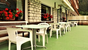 A terrace with white plastic chairs and tables, stone walls, and red flowers in window boxes. - Hotel Cristallo (Folgaria)