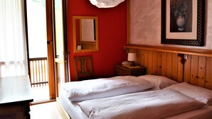 A room with a bed, a wooden nightstand, a lamp, a framed picture, and a mirror. - Hotel Cristallo (Folgaria)