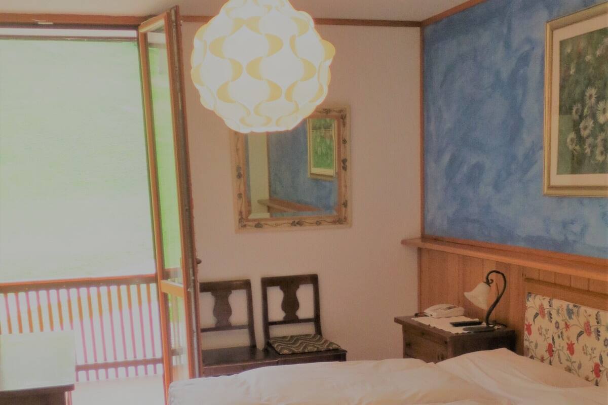 A bedroom with a bed, a nightstand, a lamp, a mirror, and a window.