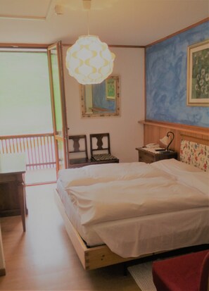A bedroom with a bed, a nightstand, a lamp, a mirror, and a window. - Hotel Cristallo (Folgaria)